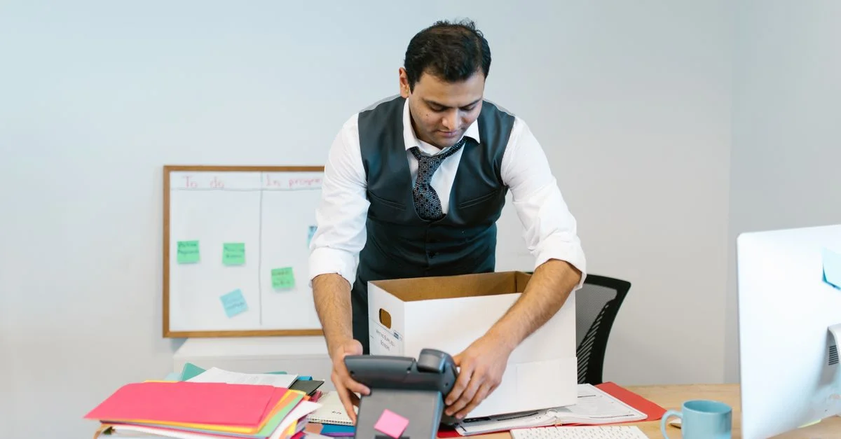 Un homme rangeant son bureau dans un environnement de bureau avec des papiers et un téléphone.