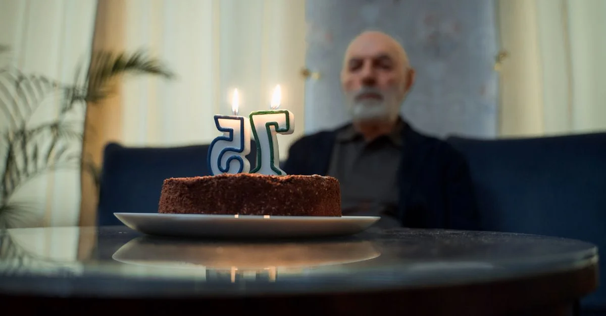Un homme âgé assis seul près d'un gâteau avec des bougies allumées marquant son 75e anniversaire.