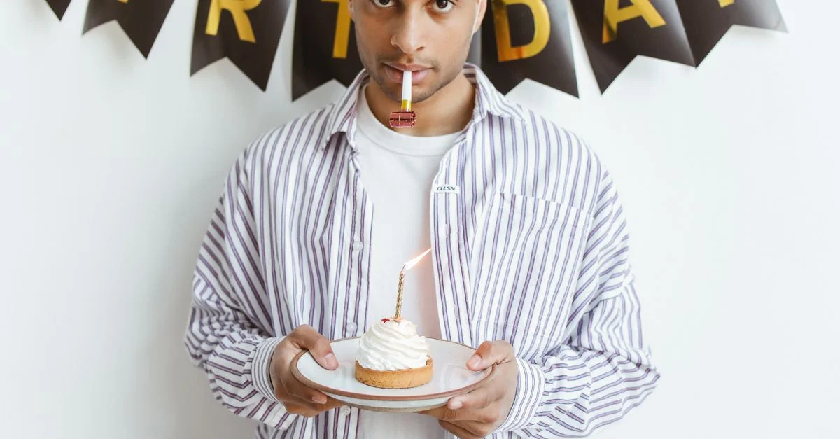 Jeune homme célébrant son anniversaire avec un cupcake et une bougie à l'intérieur.