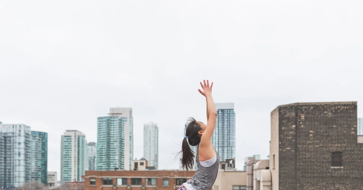 Femme adulte pratiquant le yoga en plein air sur un toit avec la skyline de la ville en arrière-plan.