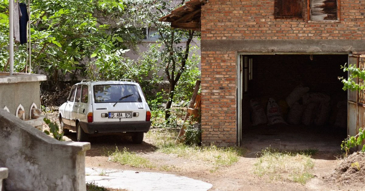 Une voiture classique garée à côté d'un garage en brique rustique dans un cadre rural luxuriant.