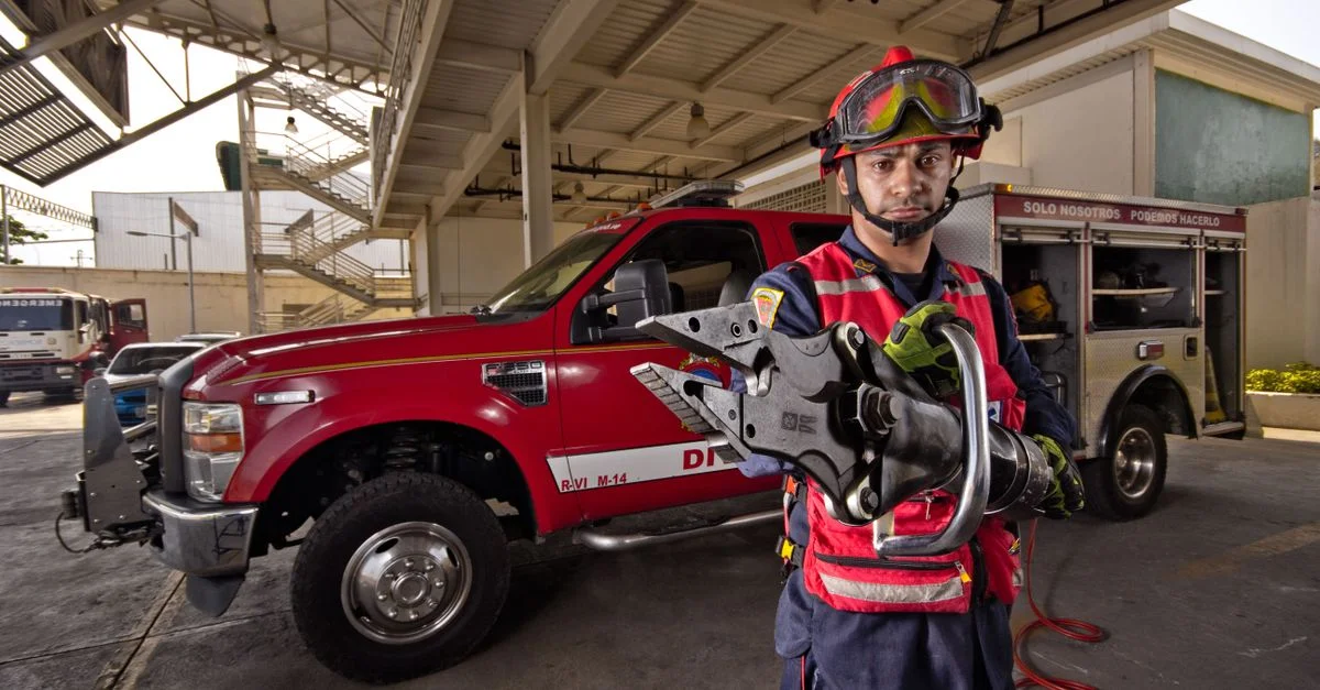 Pompier démontrant des écarteurs hydrauliques dans une caserne de pompiers. Équipement de sécurité et d'urgence présenté.