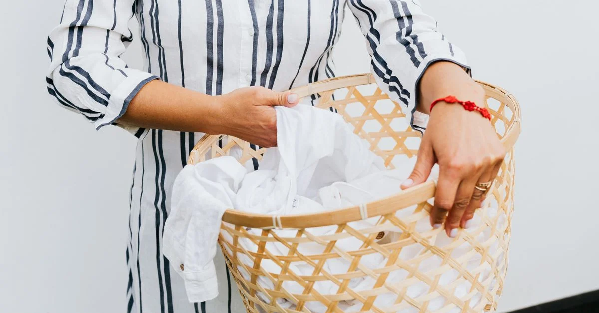 Une femme tient un panier à linge en osier avec des vêtements blancs à l'intérieur.