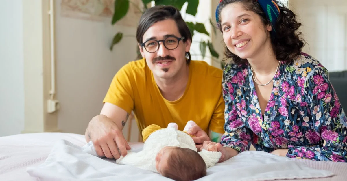 Des parents souriants avec un nouveau-né à la maison, mettant en valeur l'amour et la convivialité familiale.