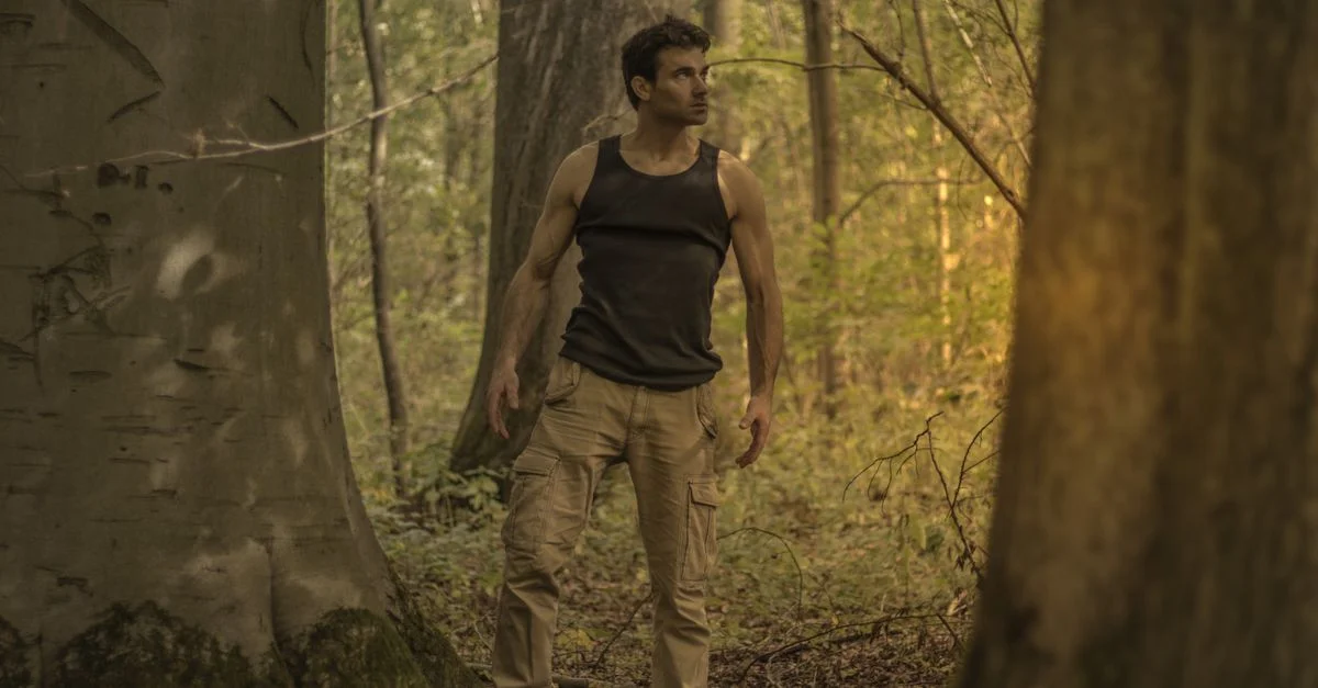 Un homme en débardeur et pantalon explorant un cadre forestier paisible.