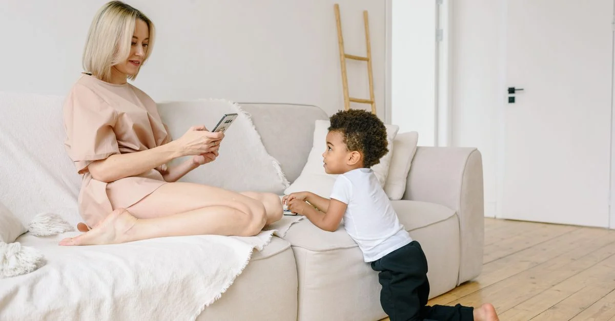 Une mère et son fils profitant d'un moment de détente à l'intérieur avec un téléphone sur un canapé confortable.