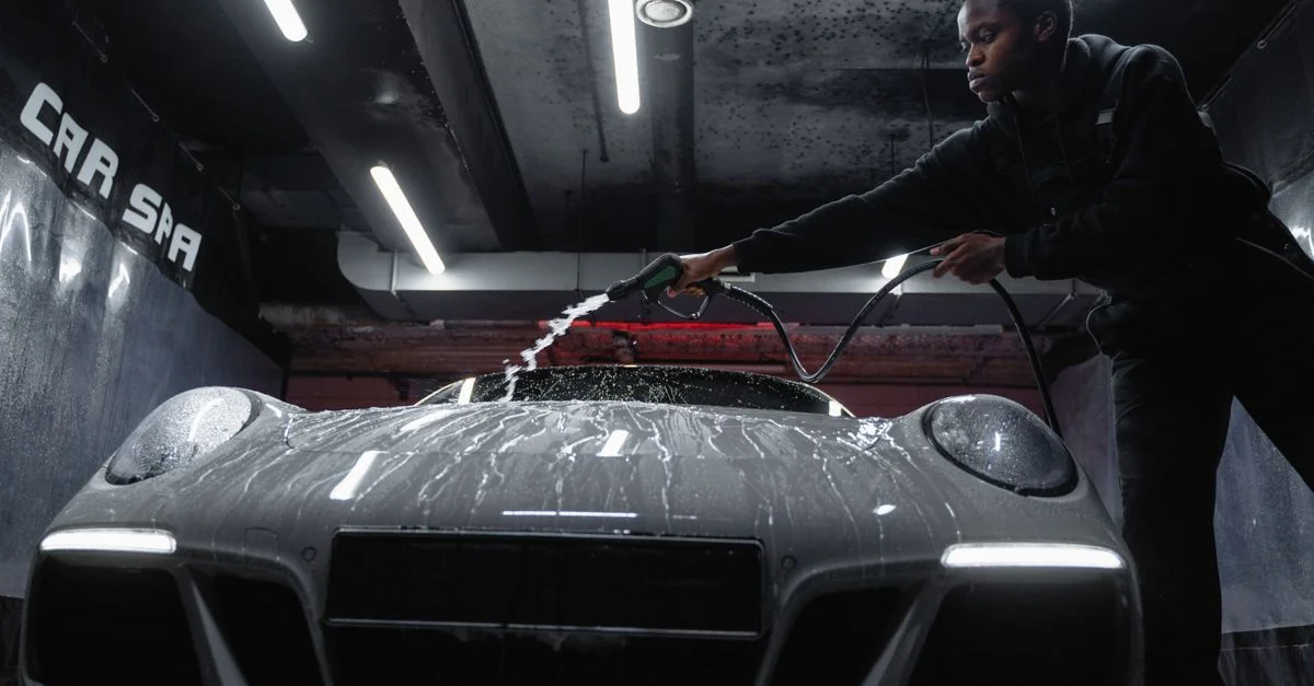 Un homme afro-américain nettoie une voiture de sport blanche dans un lavage de voiture intérieur. Perspective en contre-plongée.