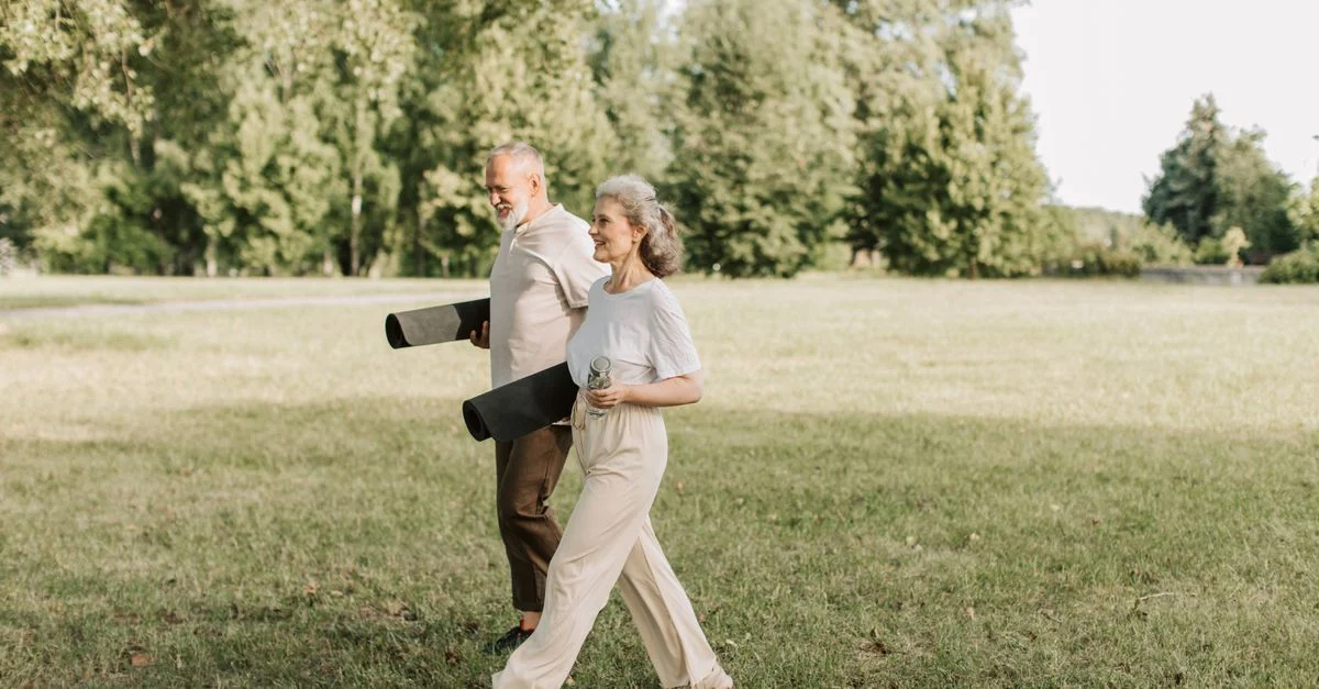 Couple âgé marchant sur l'herbe avec des tapis de yoga, profitant d'une journée ensoleillée en plein air.