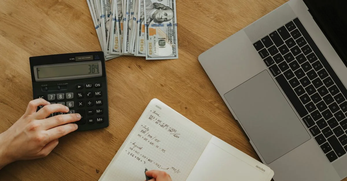 Mains utilisant une calculatrice et un carnet, planifiant des finances, avec de l'argent et un ordinateur portable sur une table en bois.